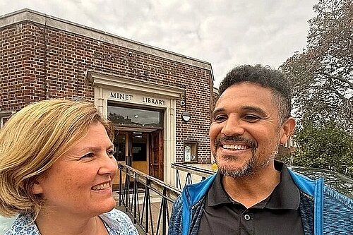 A man and a woman smiling, standing out doors in front of a brick library